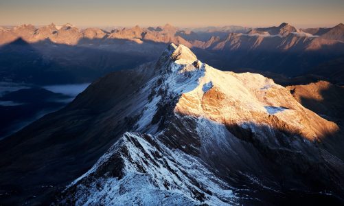 An aerial shot of snowy mountains with a clear sky in the background at daytime